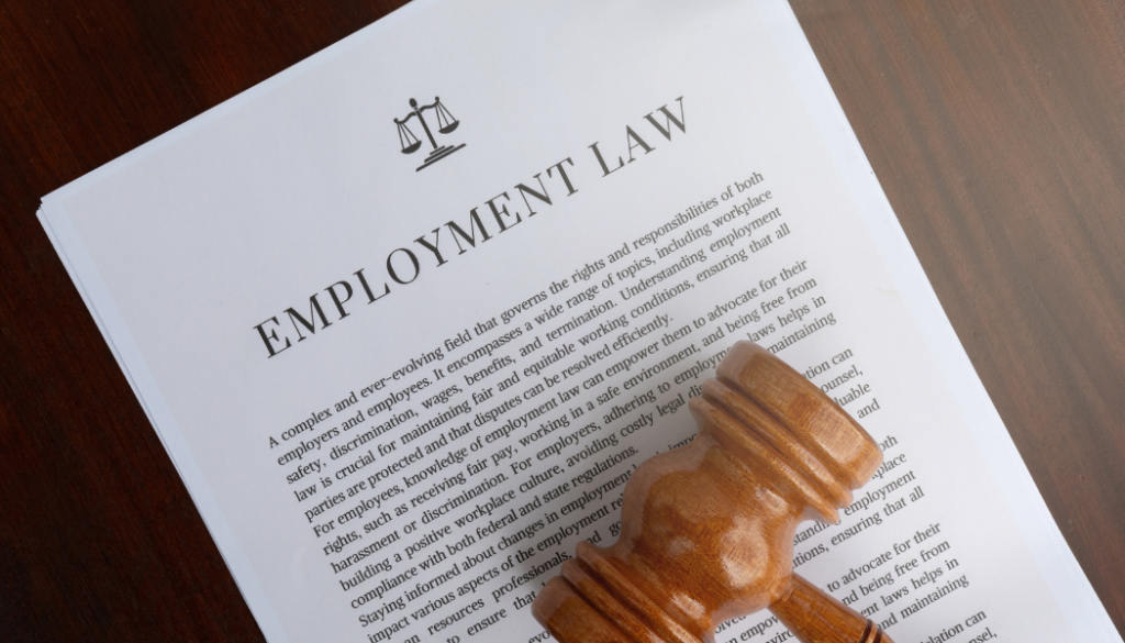 A stack of documents titled "Employment Law" with printed text, a justice scales symbol, and a wooden gavel resting on top, all placed on a wooden surface.